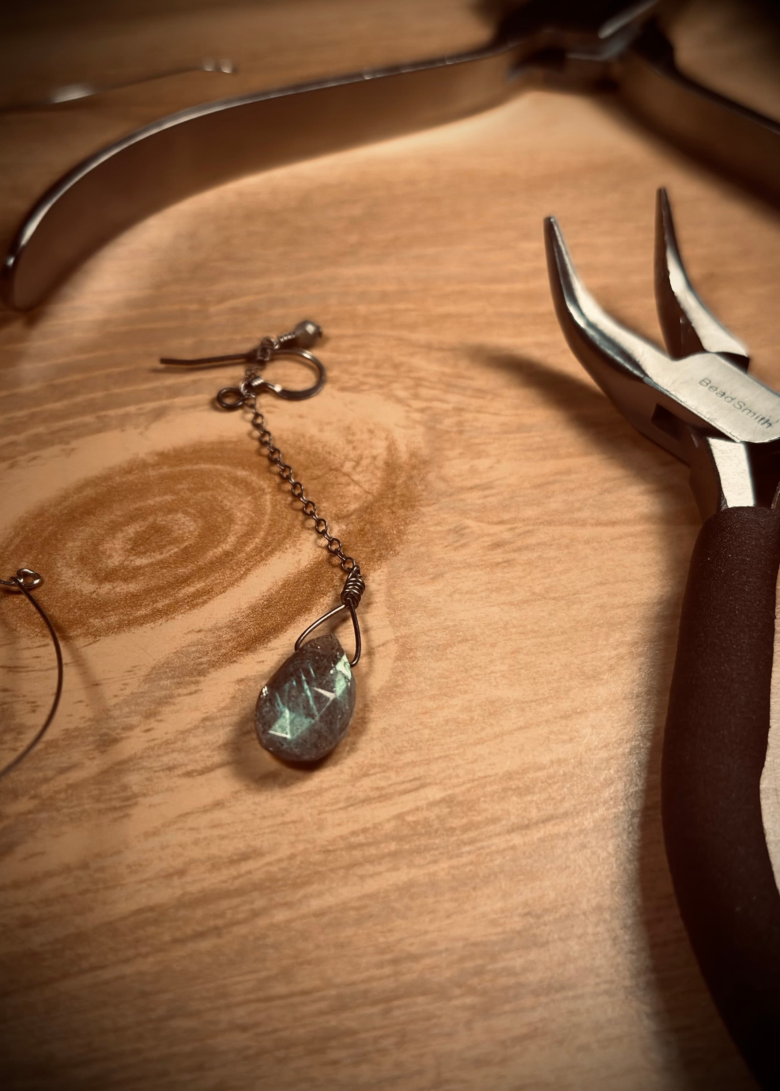 Wire-wrapped gemstone pendant with pliers on a wooden workbench
